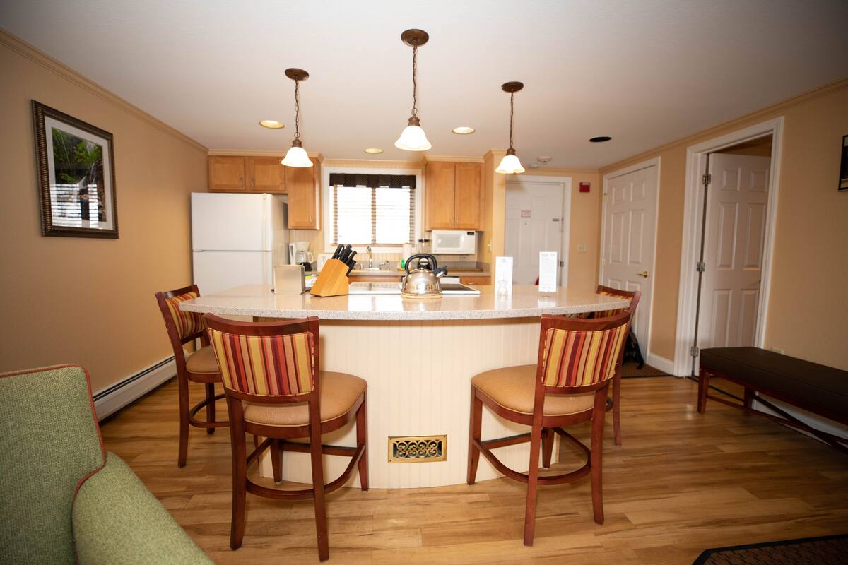A kitchen with a central island, wooden chairs, a refrigerator, and a microwave.