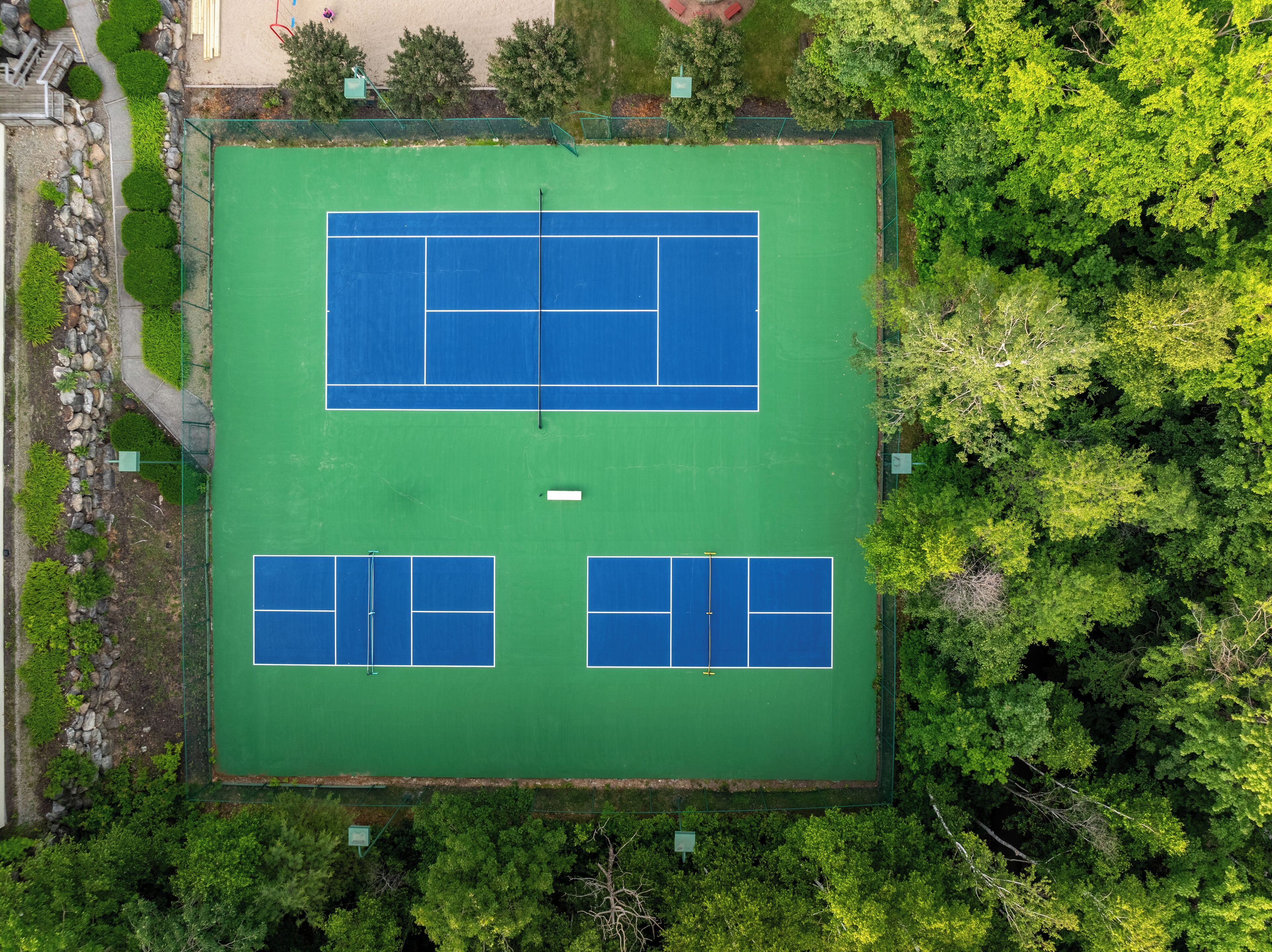 An aerial view of a tennis court surrounded by dense greenery.