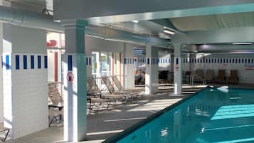 An indoor swimming pool with clear water, sunlit areas, and lounge chairs along the poolside.