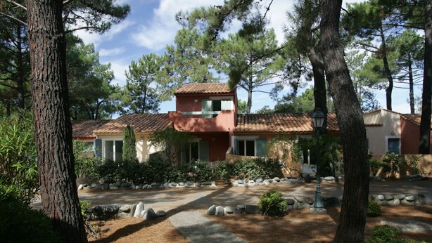 A traditional building with a tiled roof, surrounded by a landscaped garden with pine trees and a stone pathway. - Résidence Cala Bianca (Borgo)