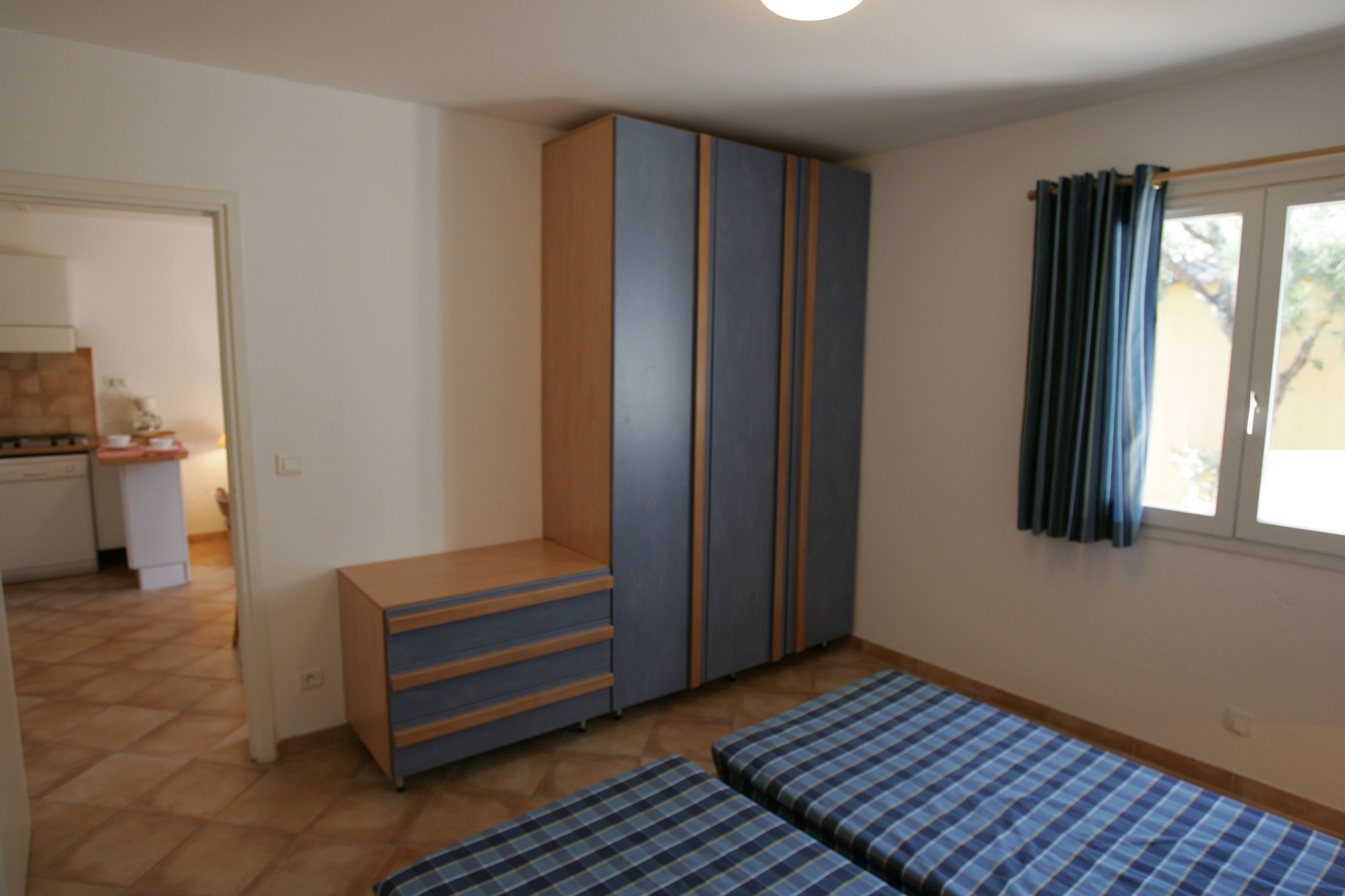 Une chambre avec une armoire, un lit et une fenêtre avec des rideaux.