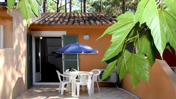 Un patio con tavolo e sedie, un ombrellone blu e una foglia verde grande.