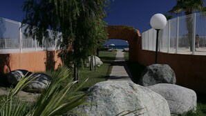 Un sendero que conduce a una zona de playa, con una cerca, rocas grandes y un poste de luz.