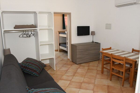 A compact living space with a sofa, a dining table with chairs, a TV, and a wardrobe.