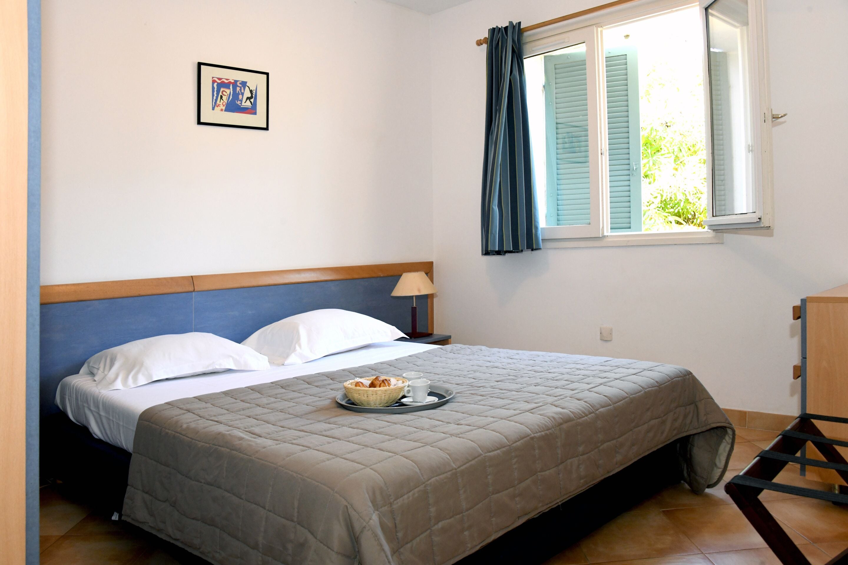 Un letto rifatto con coperta trapuntata, un comodino con una lampada e una finestra con tende.