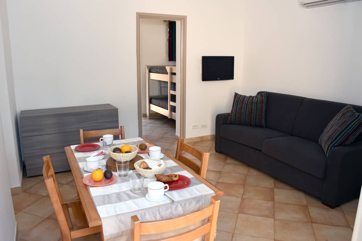 Ein Essbereich mit einem für das Frühstück gedeckten Tisch, einer Couch und einem an der Wand befestigten Fernseher.