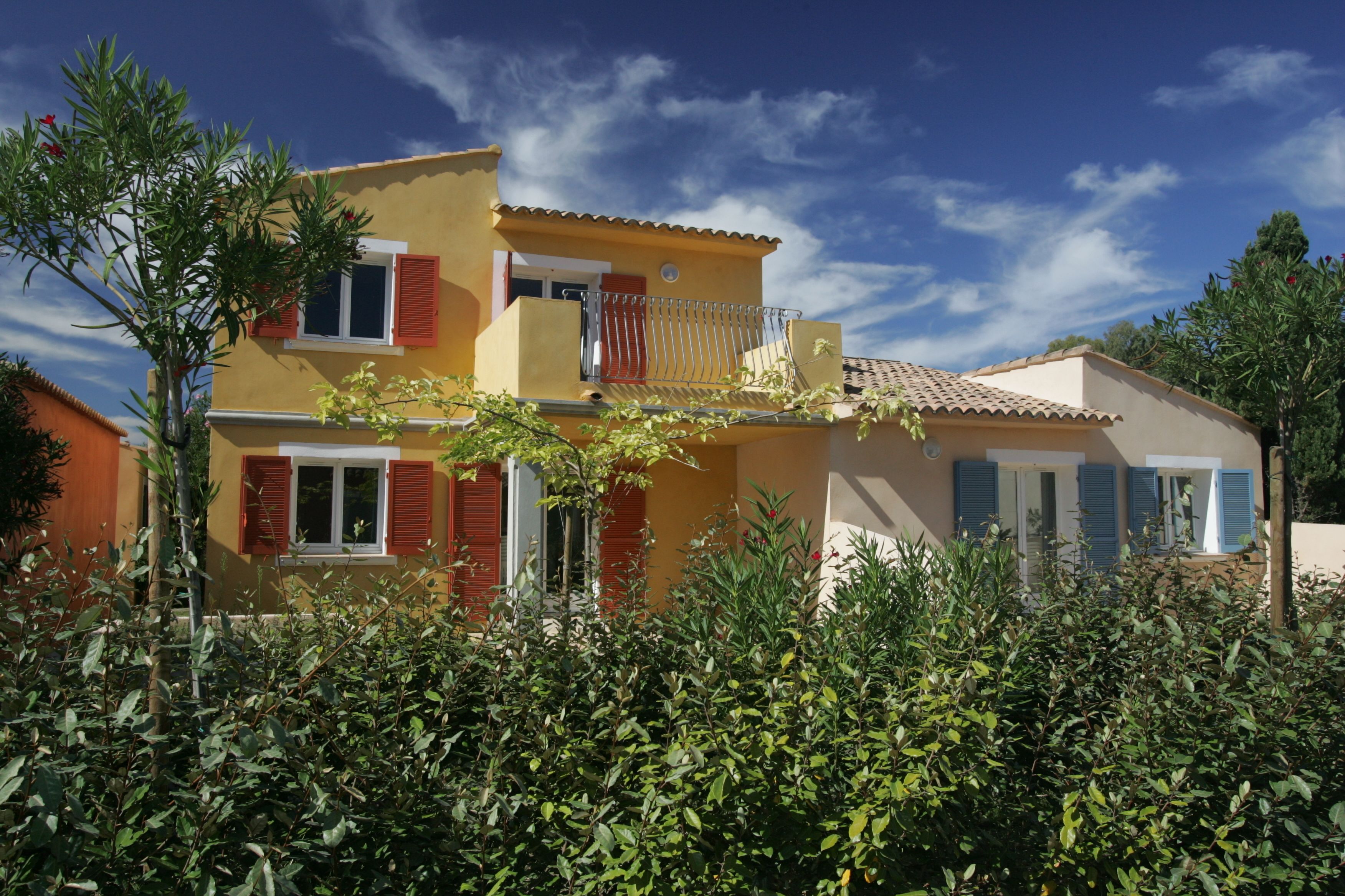 A two-story house with a balcony, surrounded by greenery.