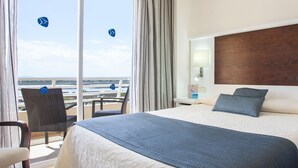 Quarto de hotel com uma cama grande, uma cadeira, uma mesinha de cabeceira e vista para o mar.