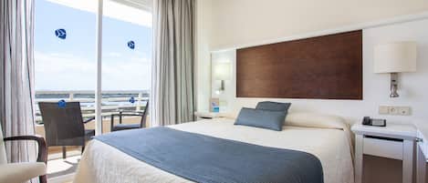 A hotel room with a bed, a desk, a chair, and a view of the beach.