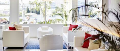 Un moderno vestíbulo de hotel con sofás blancos, una mesa de centro de vidrio y amplias ventanas que ofrecen vistas al exterior.