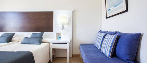 Une chambre d’hôtel avec deux lits, un bureau, un canapé bleu et un tableau encadré au mur.