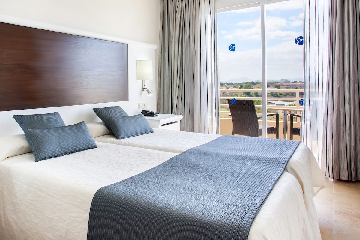 Ein Hotelzimmer mit zwei Betten, einem großen Fenster und Blick auf die Stadt.