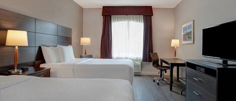 A hotel room with two beds, a desk, a chair, a television, and a window with curtains.