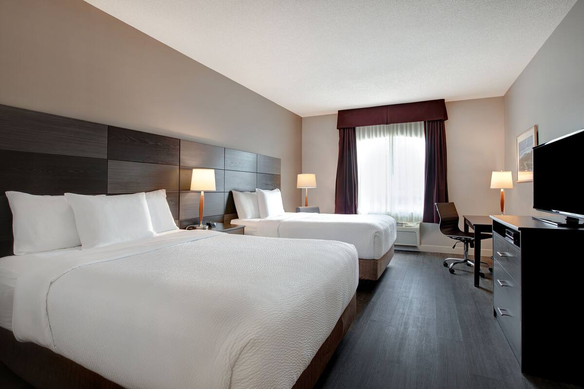 A hotel room with two beds, a desk, a chair, a television, and a window with curtains.