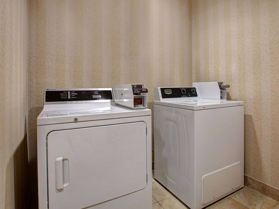 A laundry area with two white washing machines and a dryer, equipped with control panels and a paper towel dispenser.