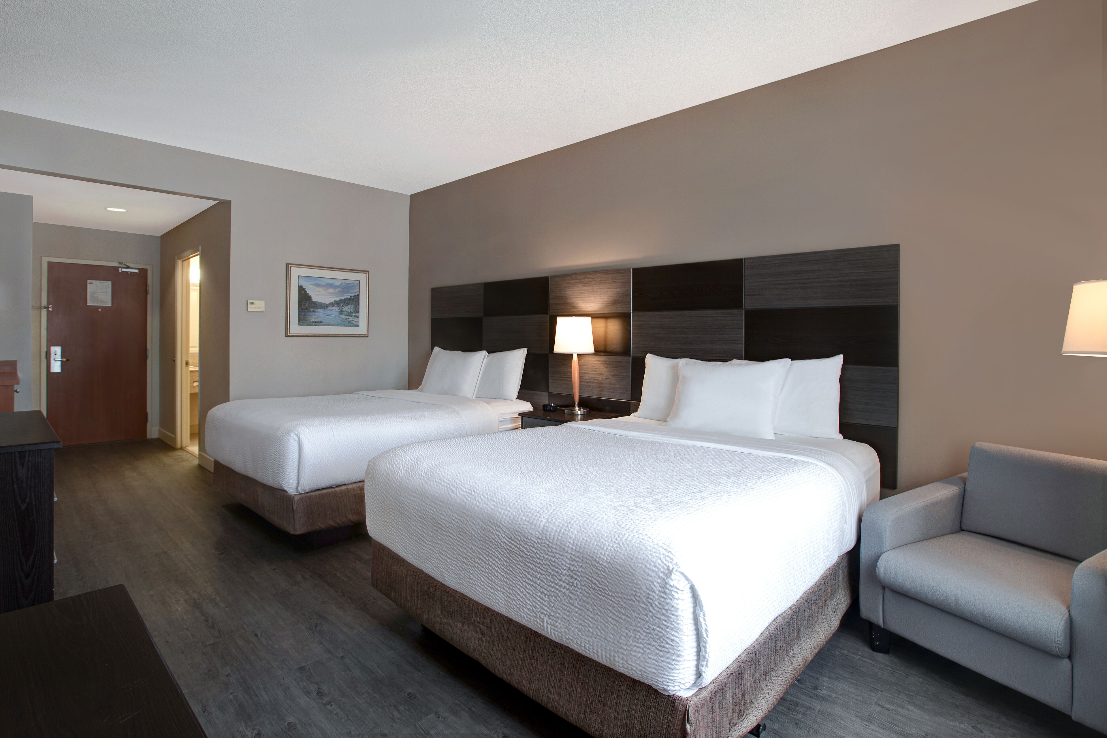 Habitació d'hotel amb dos llits, una taula de treball, una cadira i una nit falda amb una làmpada.
