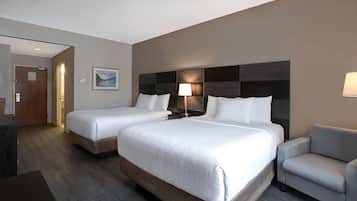 Habitación de hotel con dos camas, un escritorio, una silla y una mesita de noche con lámpara.
