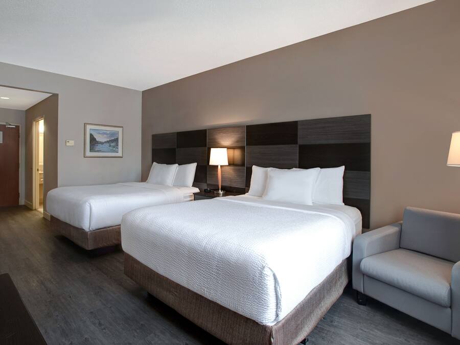 Habitación de hotel con dos camas, un escritorio, una silla y una mesita de noche con lámpara.