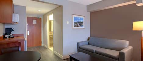 A hotel room with a sofa, a small table, a desk with a chair, and a picture on the wall.