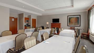 A conference room with multiple tables and chairs, a fireplace, a television, and a painting on the wall.