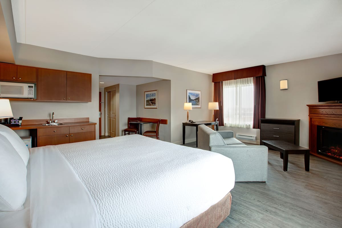 A hotel room with a large bed, a desk with a computer, a television, and a fireplace.