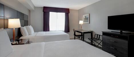 A hotel room with two beds, a desk, a television, and a chair.