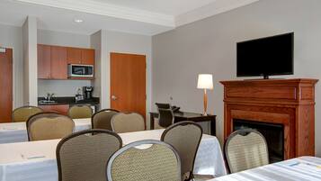A hotel room with a dining area, a fireplace, a television, and a kitchenette.