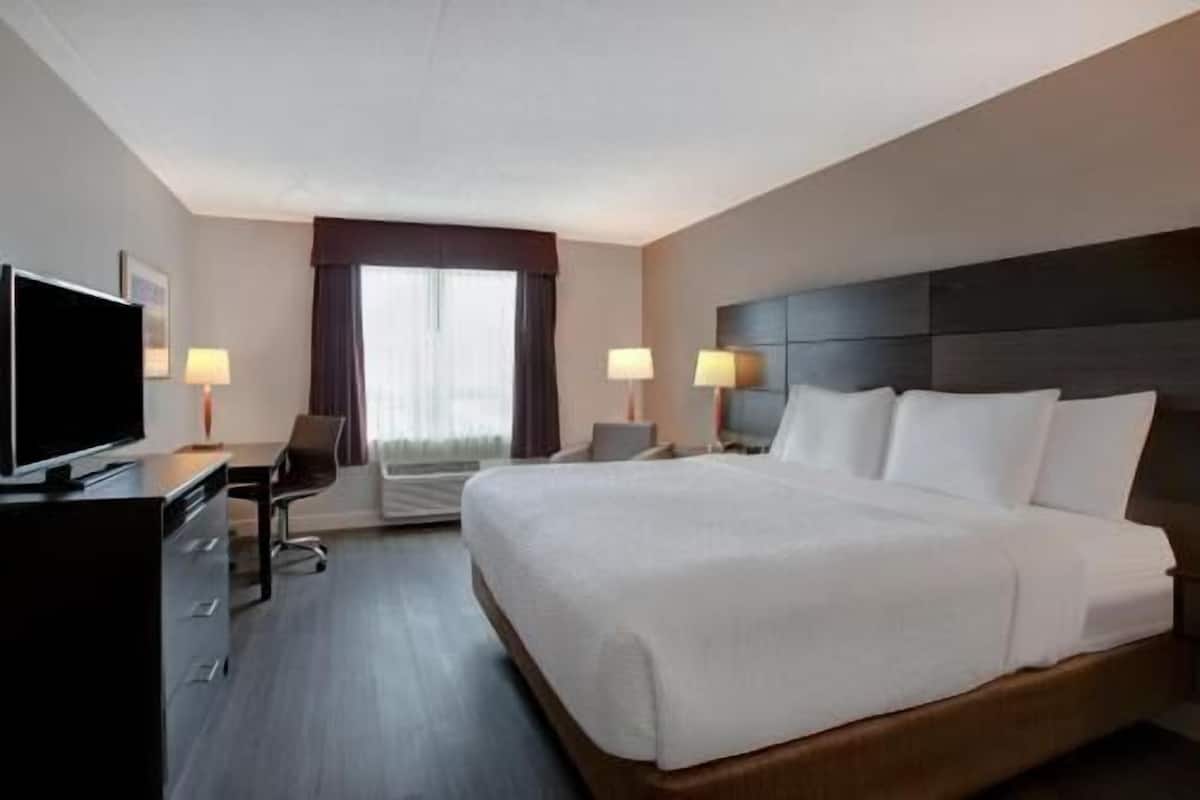 A hotel room with a large bed, a desk with a TV, two bedside lamps, and a window with curtains.