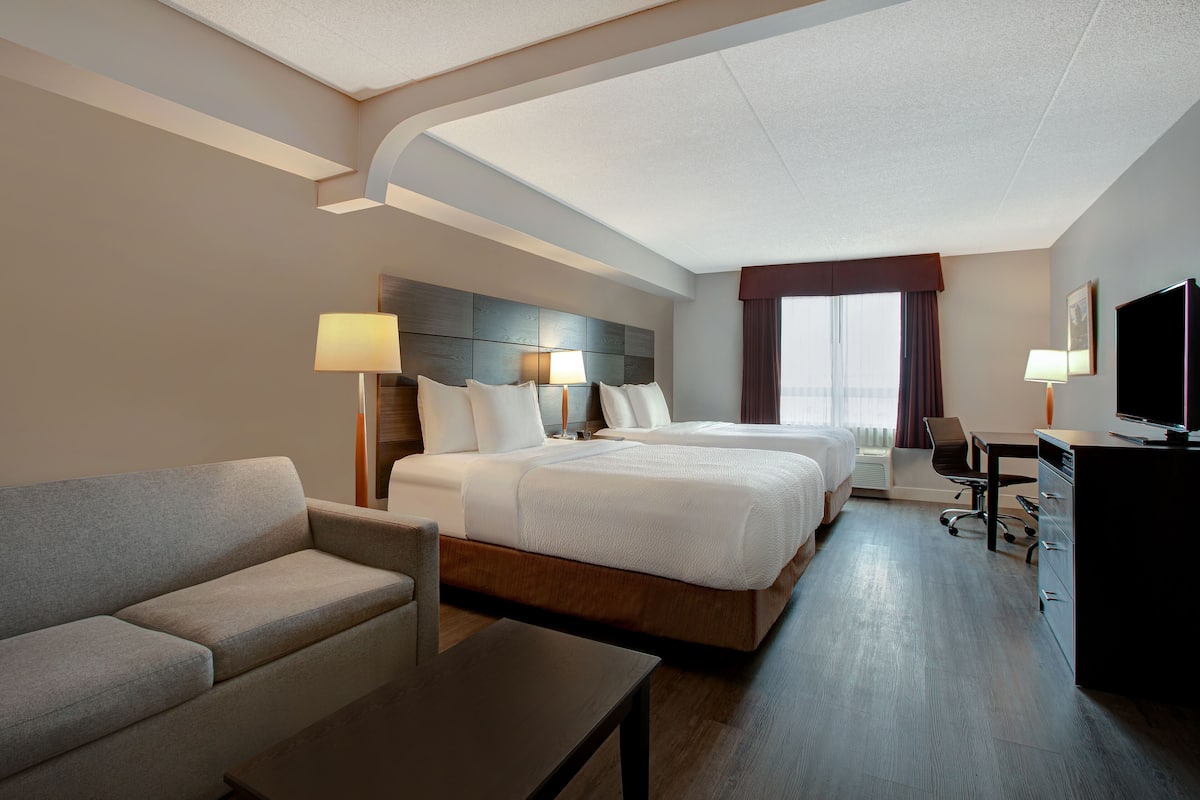 A hotel room with a large bed, a sofa, a desk, and a TV.