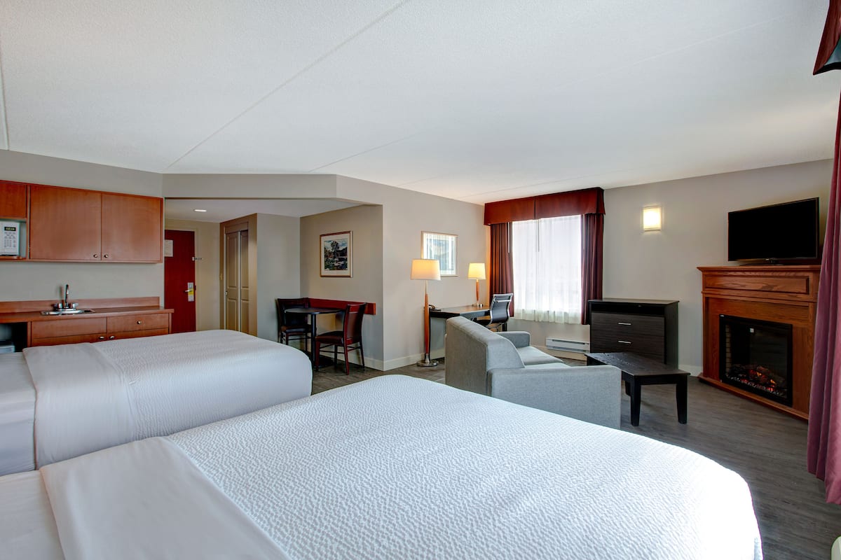 A hotel room with two beds, a desk, a chair, a television, and a fireplace.