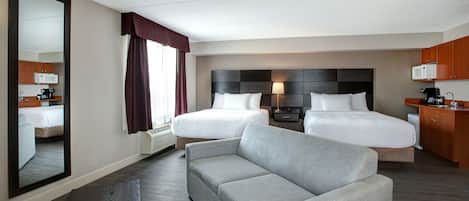 A hotel room with two beds, a sofa, a desk, a mirror, and a kitchenette.