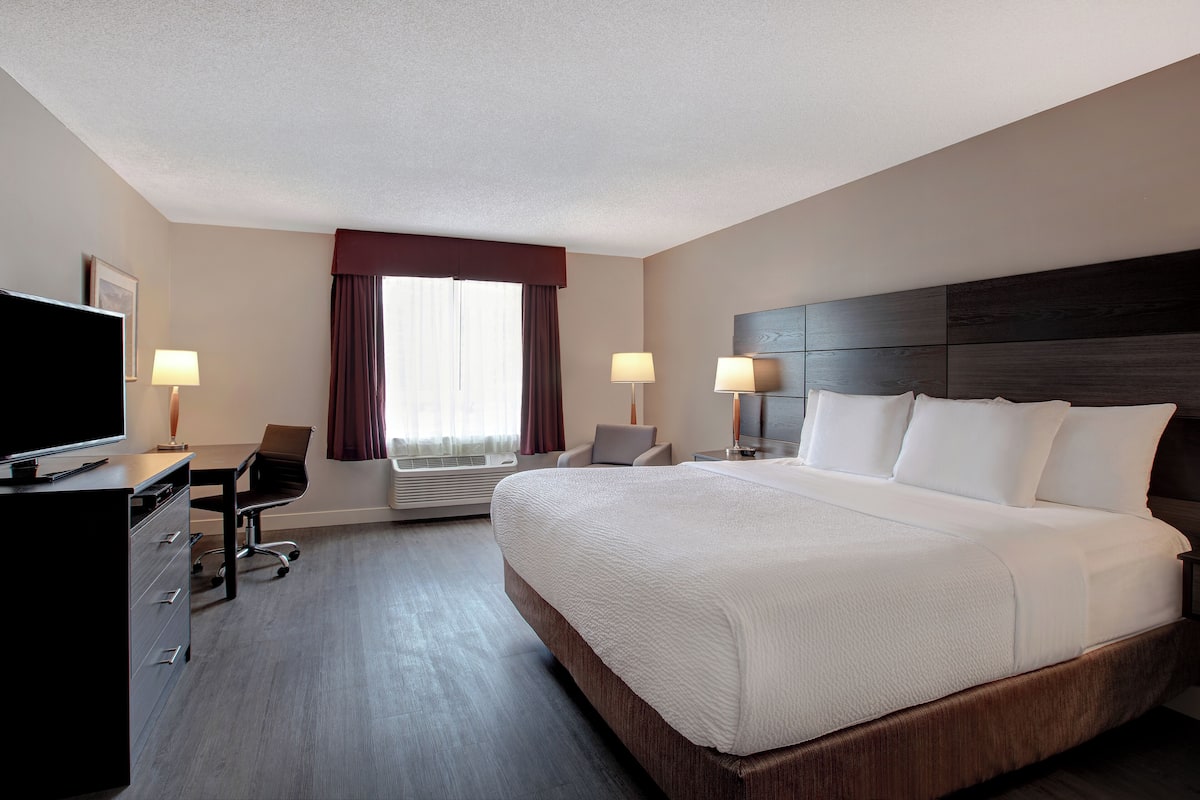 A hotel room with a large bed, a desk with a chair, a television, and two lamps.
