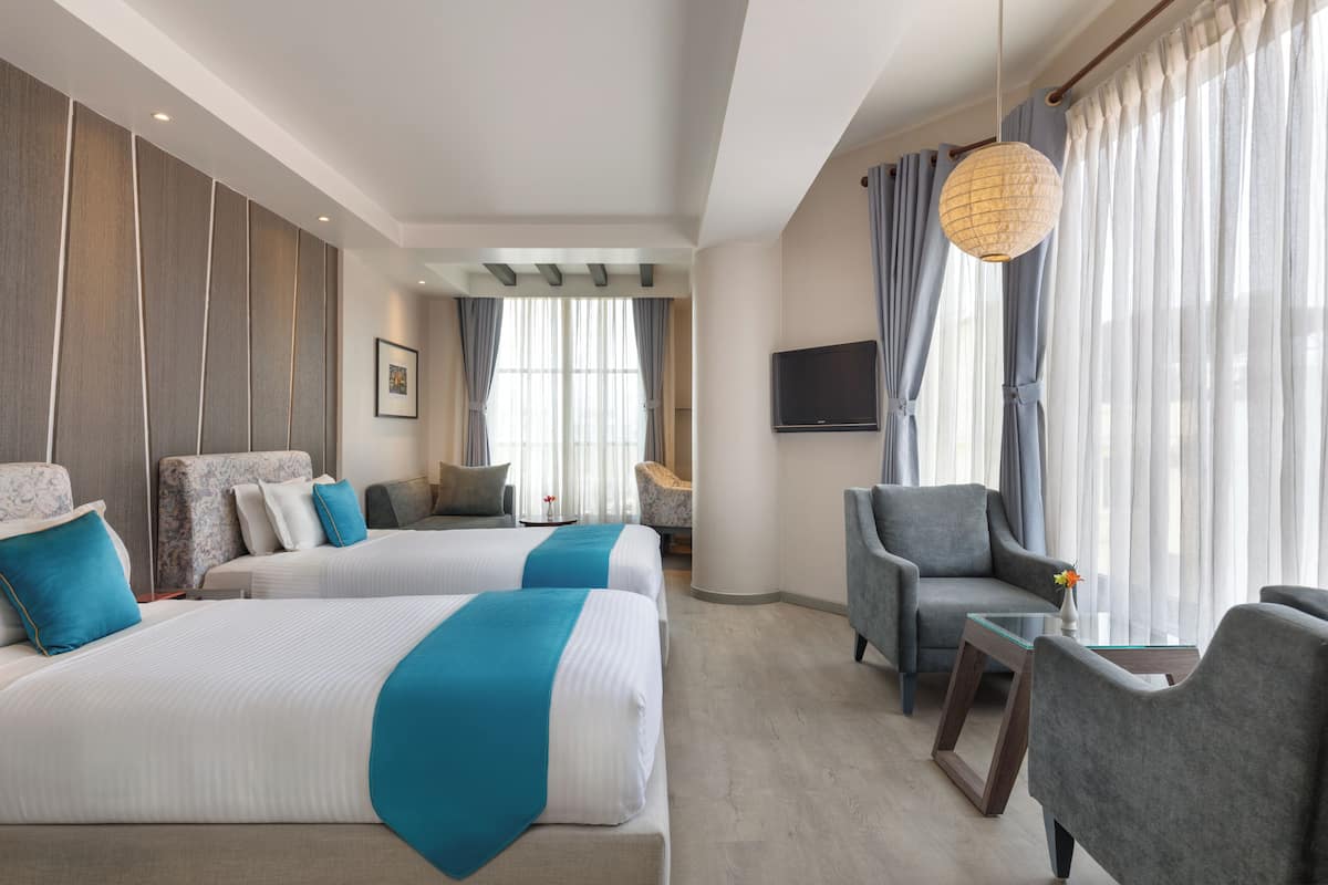 Une chambre d’hôtel avec deux lits, un canapé, une télévision et une grande fenêtre avec des rideaux.