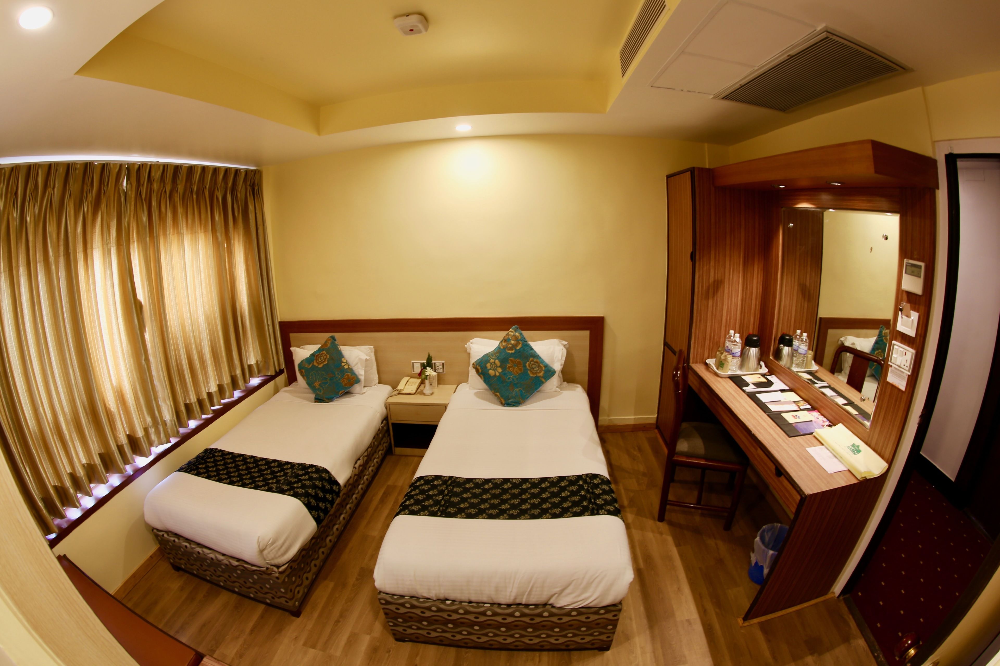 A hotel room with two beds, a desk, and a mirror.