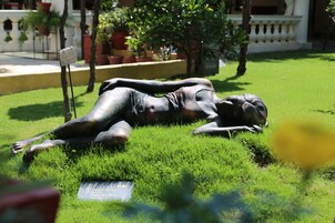 Estatua de una figura reclinada en un césped, con una placa en el frente.