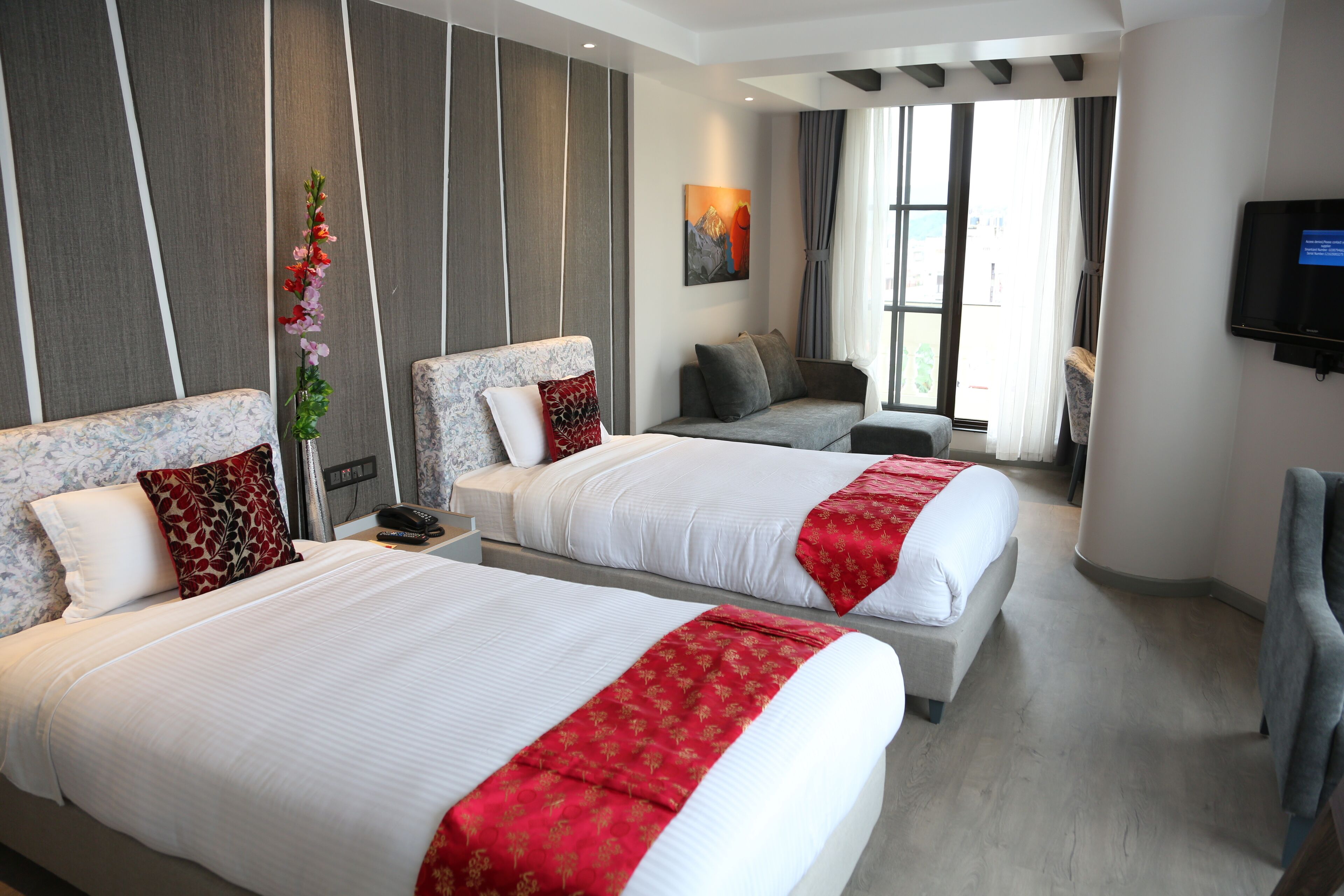 A hotel room with two beds, a sofa, a TV, and a large window.