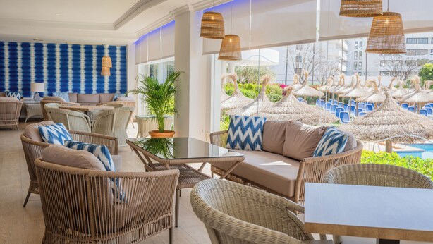 A spacious outdoor seating area with wicker furniture and a view of a pool area with umbrellas. - Grupotel Maritimo (Alcúdia)