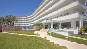 A modern hotel with a curved facade, multiple balconies, and a well-maintained lawn with decorative lanterns.