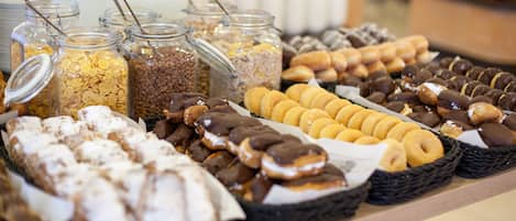 A buffet with various food items including cereals, pastries, and donuts.