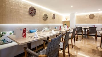 Een eetruimte met een lange tafel, meerdere stoelen en een bank. Er liggen placemats, bestek en een menustandaard.