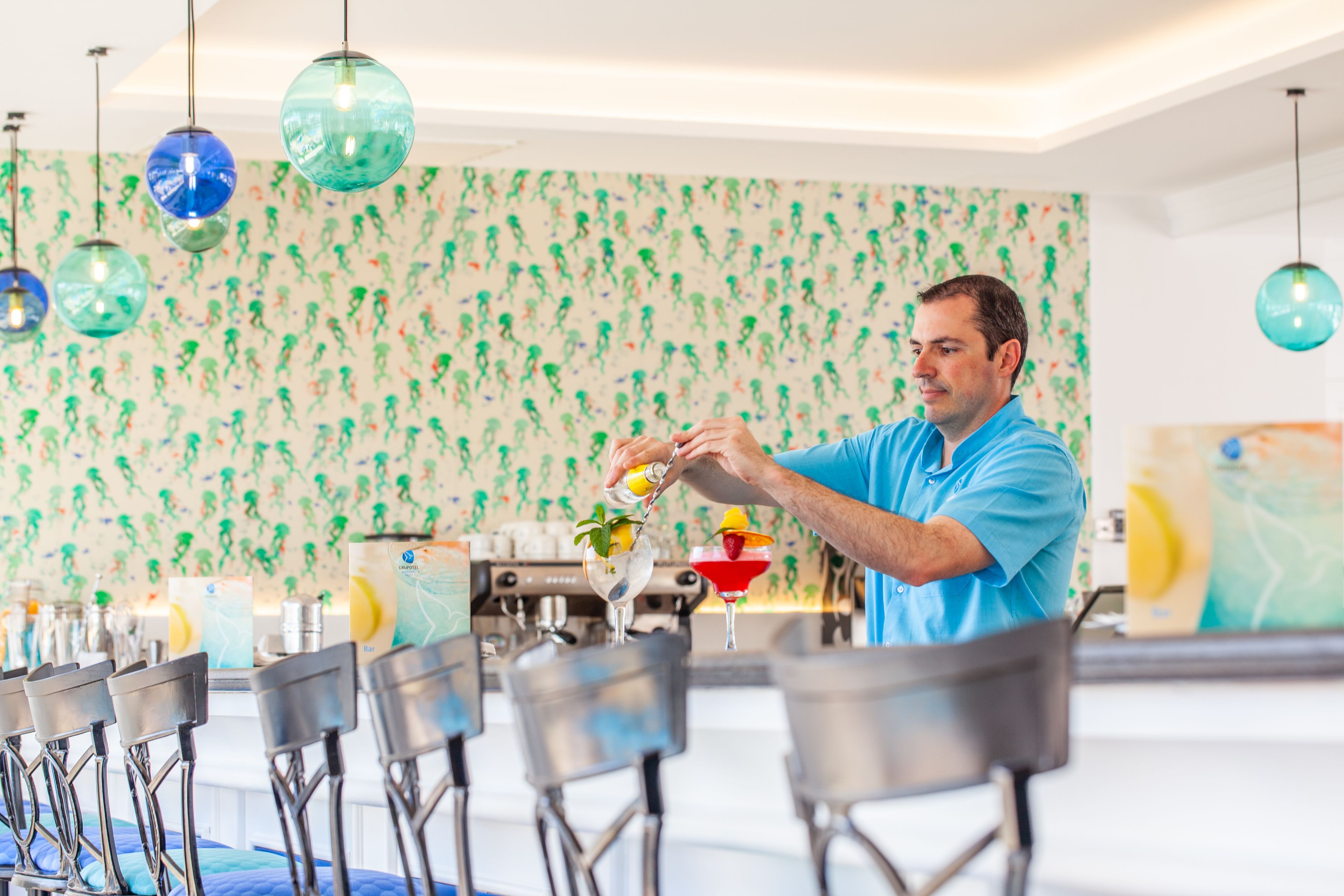 Angolo bar con un barista che prepara cocktail, sgabelli da bar e carta da parati decorata.