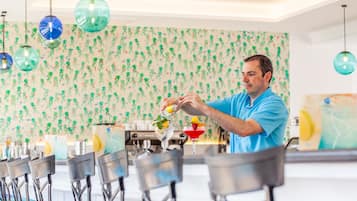 A bar area with a bartender preparing drinks, bar stools, and a patterned wallpaper background.