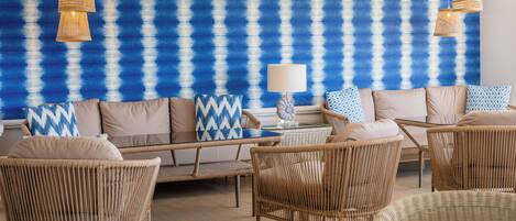 Une pièce meublée de mobilier en osier, avec un mur orné d’un motif bleu et des lampes en osier suspendues au plafond.