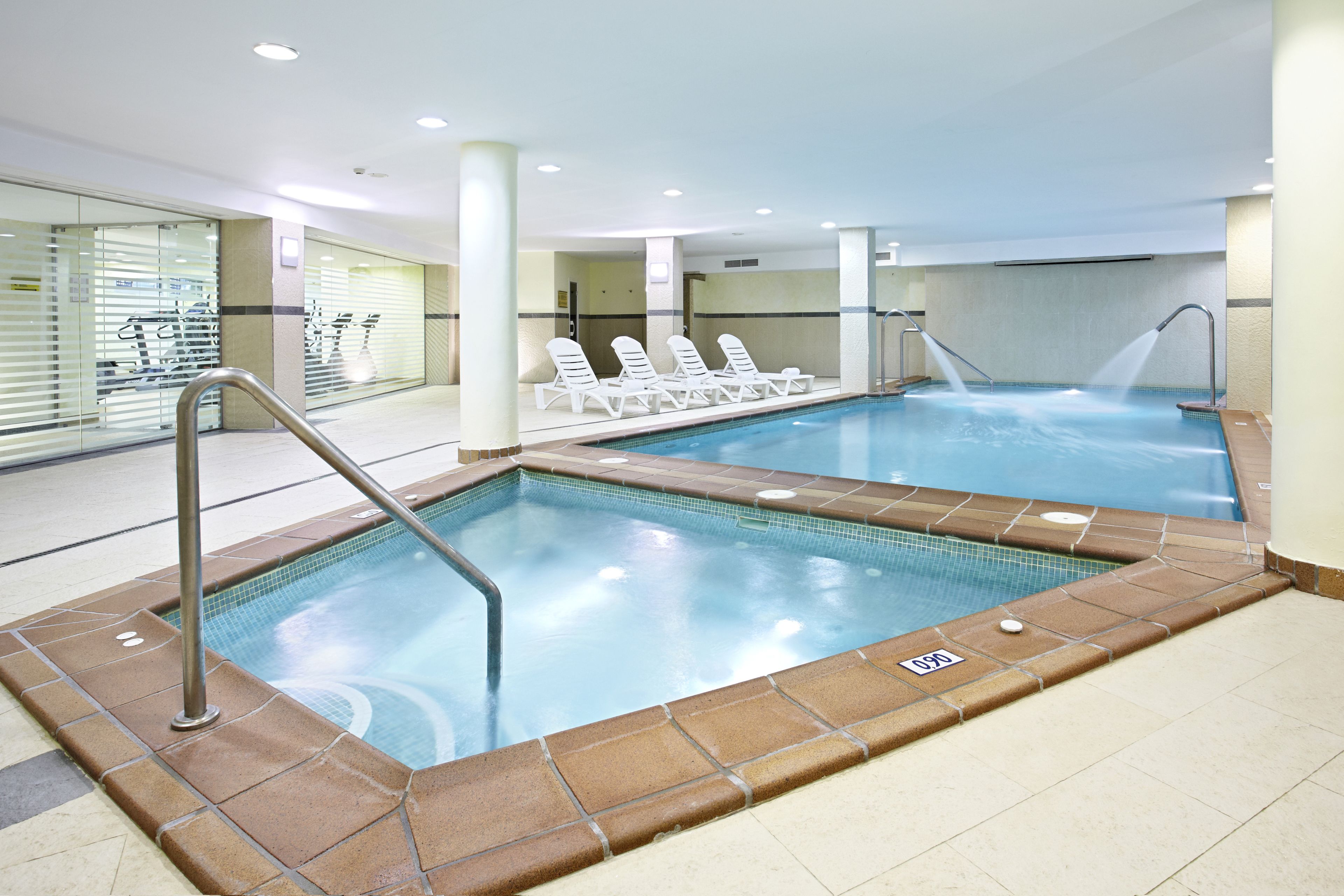 An indoor swimming pool with clear water, a diving board, and lounge chairs.