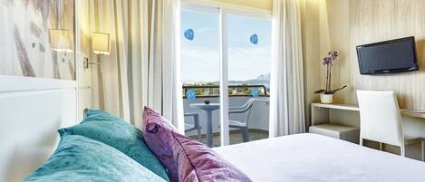 A hotel room with a bed, a desk, a TV, and a balcony with a view.