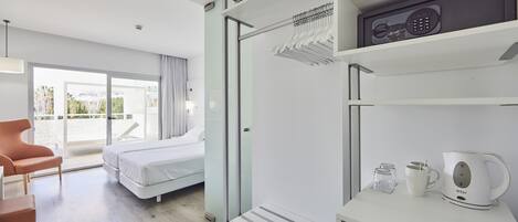 A modern hotel room with a bed, a seating area, a coffee maker, and a view of the outdoors.
