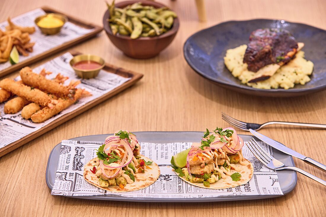Una taula plena de plats diversos, com tacos, patates fregides i una entrecot.