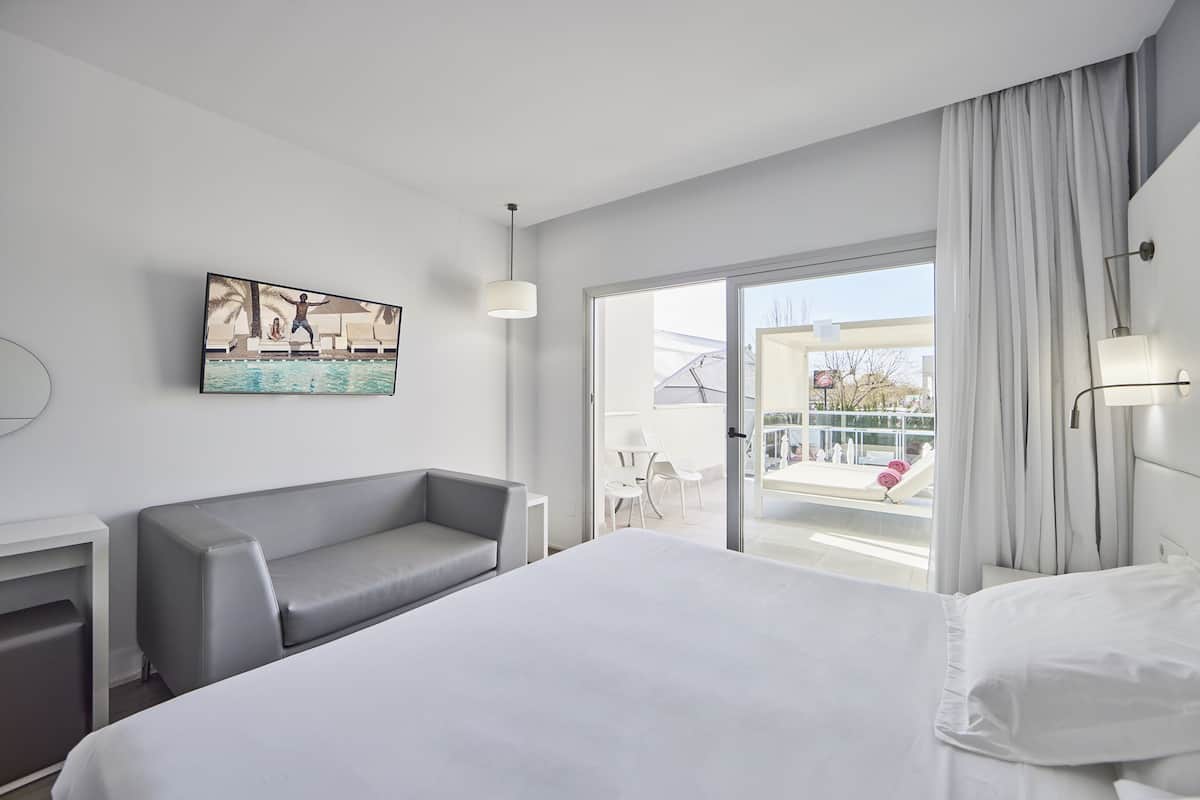 Une chambre d’hôtel moderne avec un grand lit, un canapé gris, une petite table et un tableau au mur.