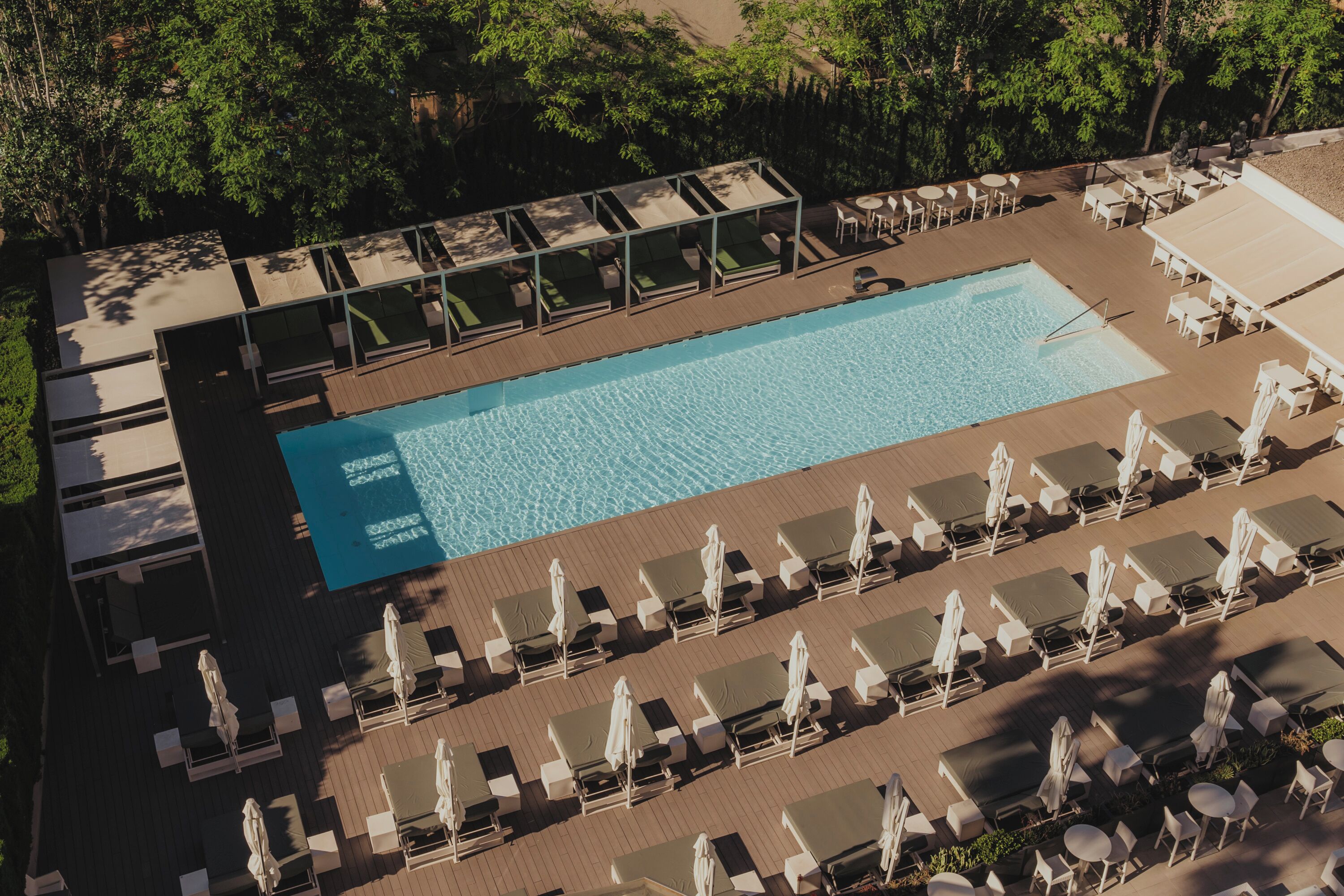 Vista aérea de un área de piscina de hotel con tumbonas, sombrillas y una alberca.