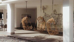 Ein moderner Außenbereich mit drei von der Decke hängenden Korbstühlen, einem Betonboden und einem großen Stadtbild-Wandgemälde.